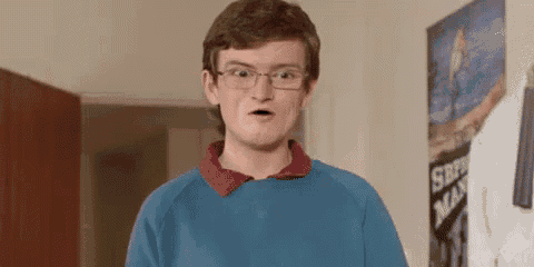 a young man wearing glasses and a blue sweater is making a funny face in front of a poster .
