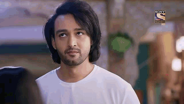 a man with long hair and a beard is wearing a white shirt and looking up at something .
