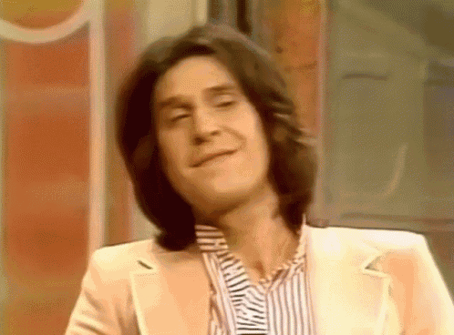 a man with long hair is wearing a white suit and striped shirt .