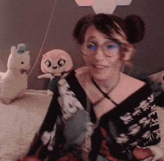 a woman wearing glasses is holding a stuffed animal and smiling