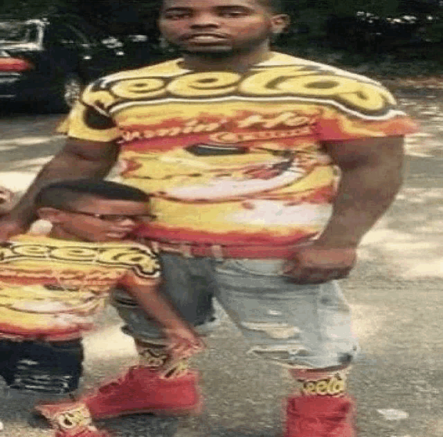 a man wearing a cheetos shirt stands next to a child