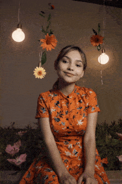 a woman in an orange floral dress is surrounded by flowers and bulbs