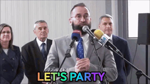 a man in a suit and tie speaking into a microphone with the words let 's party below him