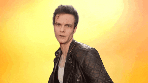 a man wearing a leather jacket with a yellow background looks at the camera