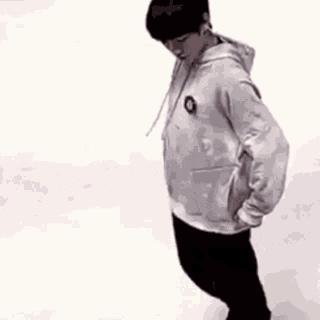 a young man wearing a white hoodie and black pants is standing on a snowy surface .