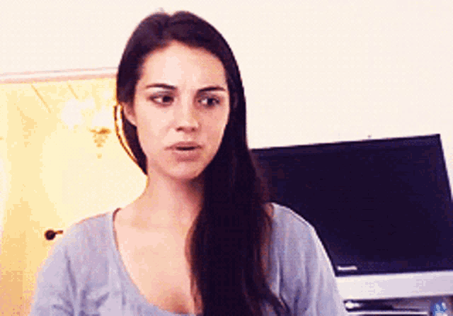 a woman in a grey shirt stands in front of a television