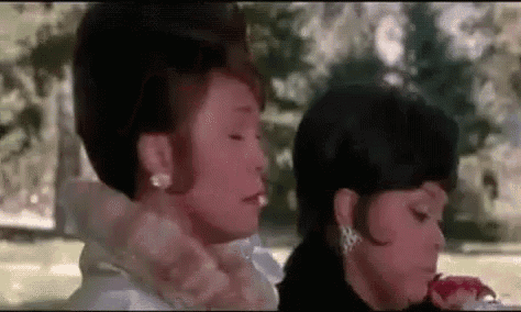two women are sitting next to each other in a park . one of the women is holding a flower in her hand .