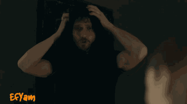 a man in a black shirt is looking at himself in a mirror with ecyam written on the bottom right