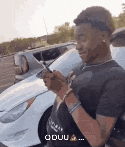 a man is standing in front of a white car holding a cell phone .