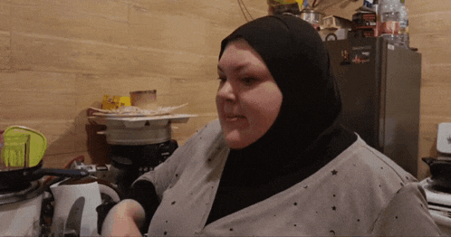 a woman wearing a black hijab is standing in front of a fridge that says ' samsung ' on it