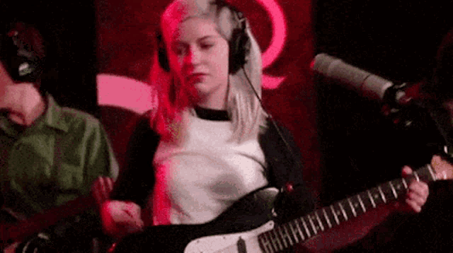 a woman wearing headphones is playing a guitar in front of a microphone in a recording studio .