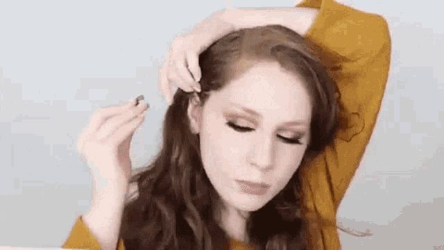 a woman is holding a hair clip in her hand and applying makeup to her face .