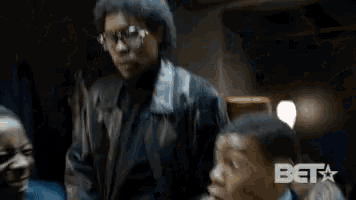 a group of men are standing around each other in a dark room and one of them is making a funny face .