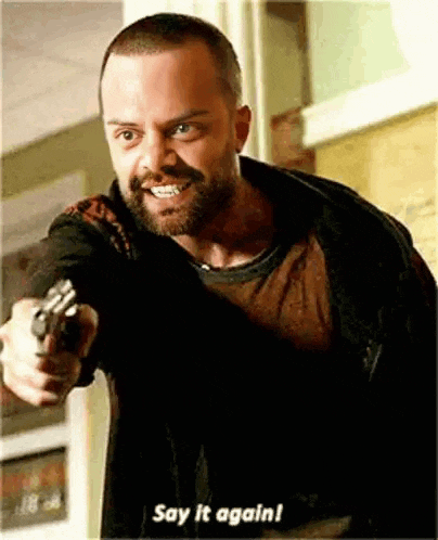 a man with a beard is pointing a gun at the camera and says `` say it again '' .