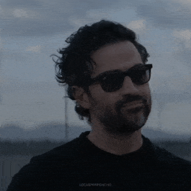 a man wearing sunglasses and a black shirt with the word locasporponcho on the bottom right