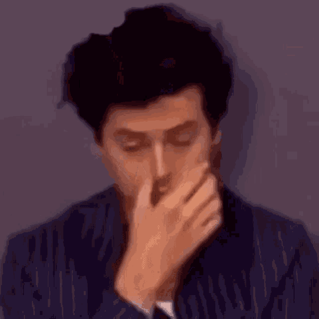 a man in a blue striped suit is covering his nose with his hand .