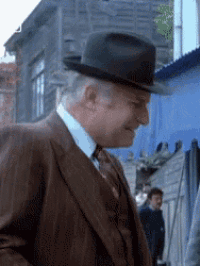 a man in a suit and hat is standing in front of a blue building