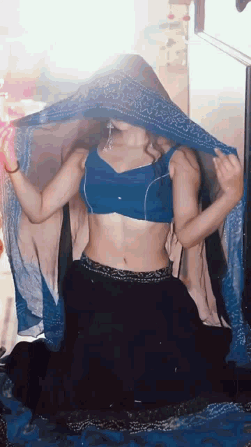 a woman in a blue crop top and black skirt is covering her face with a blue scarf