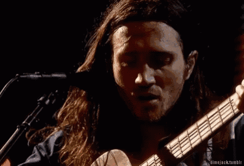 a man with long hair is singing into a microphone while holding a guitar .