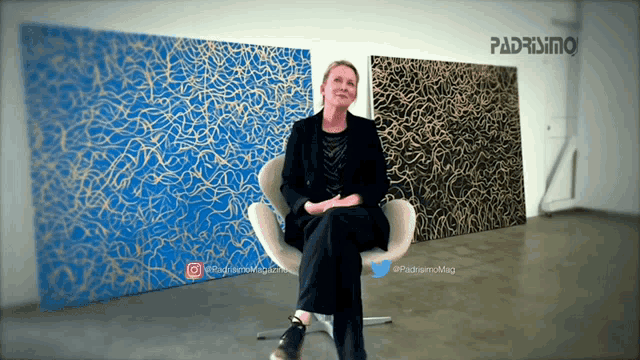 a woman sits in a chair in front of paintings with the word padremio on the bottom right