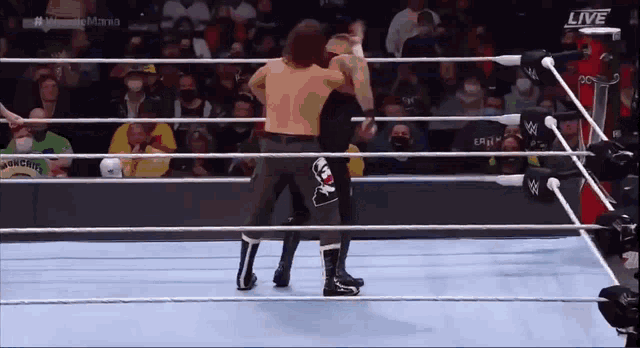 two men are wrestling in a wrestling ring while a crowd watches .