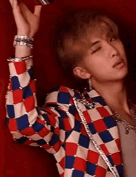 a close up of a person wearing a red , white , and blue checkered jacket and earrings .
