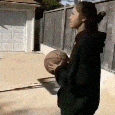 a woman in a black hoodie is holding a basketball in her hands