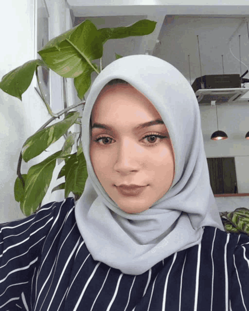 a woman wearing a striped shirt and a gray hijab looks at the camera