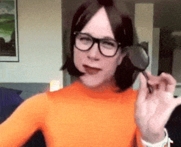 a woman wearing glasses and an orange shirt is holding a magnifying glass in her hand .