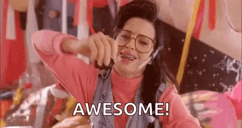 a woman with braces on her teeth is wearing a pink shirt and a denim vest and says `` awesome '' .