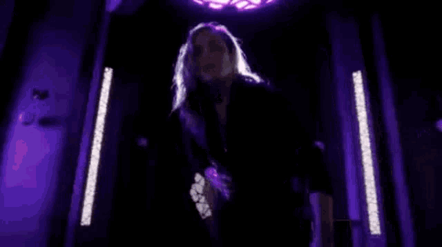 a woman in a black dress is standing in front of a purple light in a dark room .