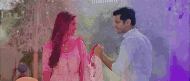 a man and woman are standing next to each other and looking at each other . the woman is wearing a pink dress .