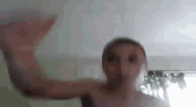 a man without a shirt is standing in front of a window and making a funny face .