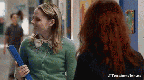 two women are standing next to each other in a hallway and one is holding a folder .