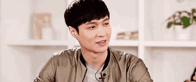 a young man wearing a jacket and a microphone is sitting in front of a bookshelf .