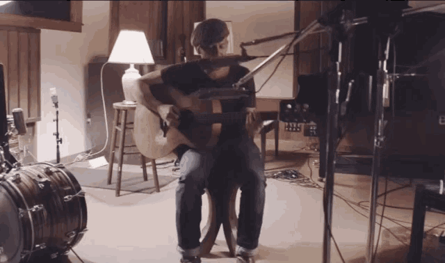 a man playing a guitar in front of a microphone with a drum in the background