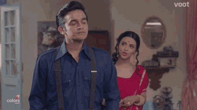 a man in a blue shirt and suspenders stands next to a woman in red
