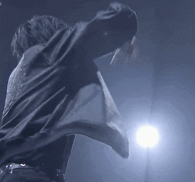 a man is standing on a stage with his arms outstretched in front of a microphone .