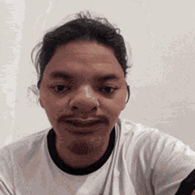 a man with a beard is wearing a white t-shirt and making a funny face .