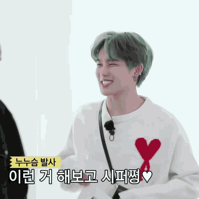 a young man with green hair wears a white sweater with a red heart on it