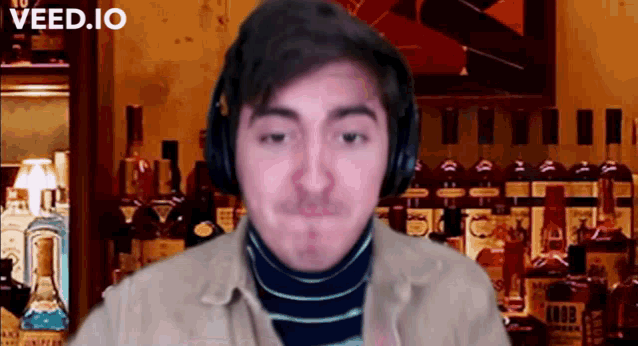 a man wearing headphones is standing in front of a bar filled with bottles of liquor .