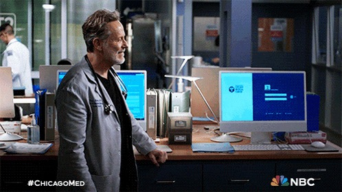 a man in a lab coat is standing in front of a computer with the nbc logo on the bottom right