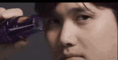 a man is holding a bottle of lotion in front of his eye .