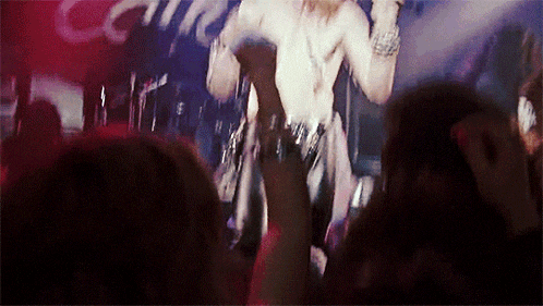 a man without a shirt is singing into a microphone in front of a crowd with their hands in the air
