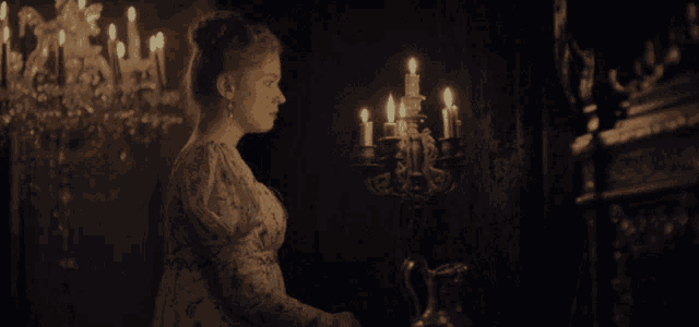a woman stands in front of a candelabra with candles lit