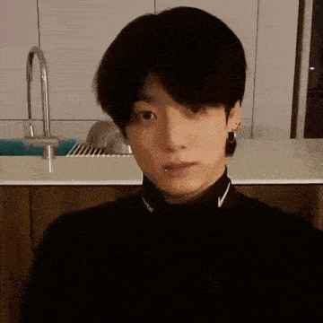 a young man wearing a black turtleneck and a nike necklace looks at the camera