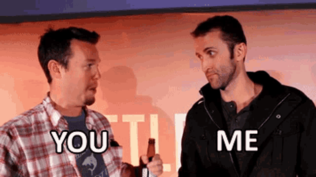 two men are standing next to each other and one of them is holding a bottle of beer and the other is saying you me