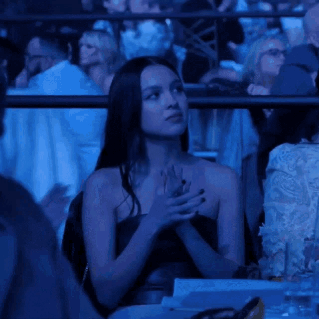 a woman in a strapless dress sits in a dark room with her hands folded
