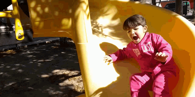a little girl wearing a pink everlast shirt is playing on a yellow slide