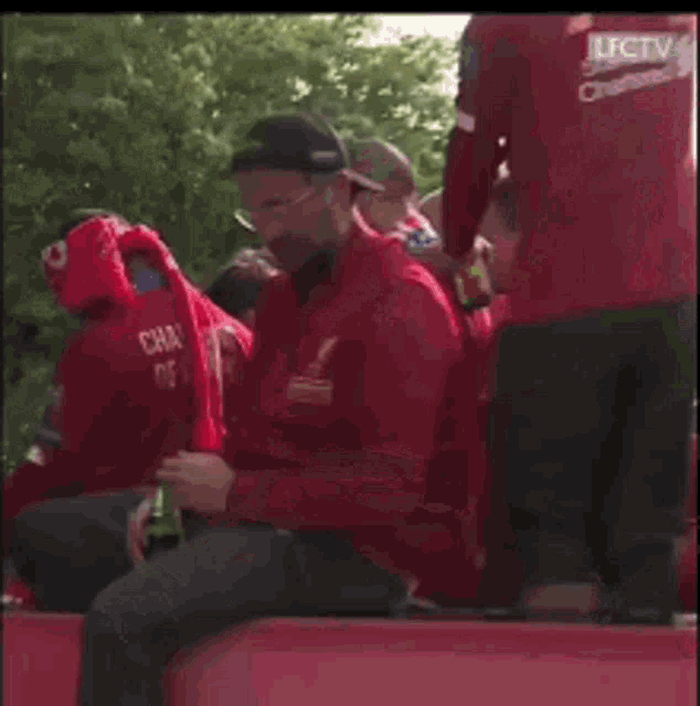 a man in a red shirt is looking at his phone while sitting in a crowd .